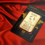 A 50g fine gold bar displayed elegantly on a rich red fabric background, symbolizing wealth and luxury.